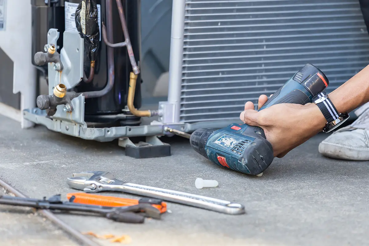 Drill being used on an HVAC system with other tools on the ground next to it.